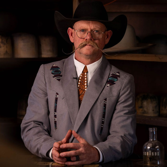 A man, Chaz Mitchell, standing in front of his hat bar and his hat tools.
